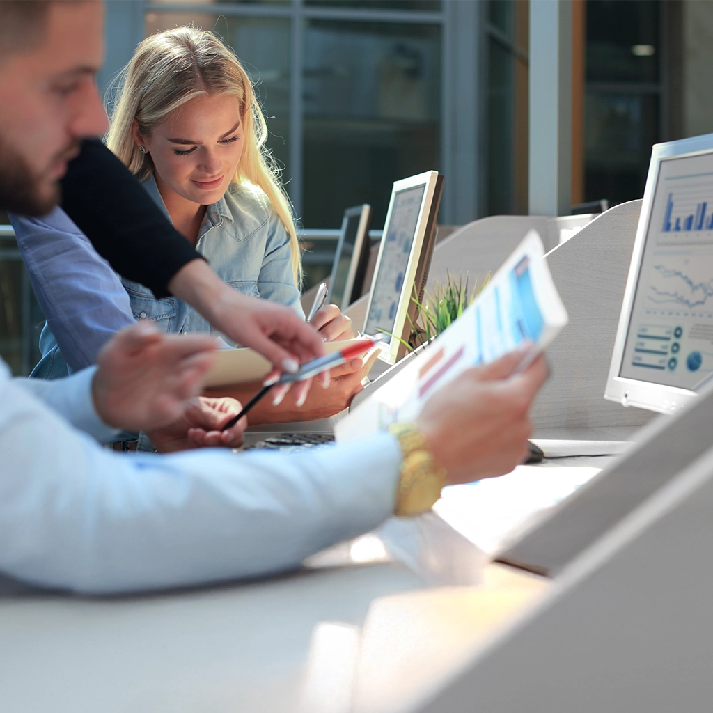 A woman and a man sitting at the desk in the office, talking, and looking at some statistics.
