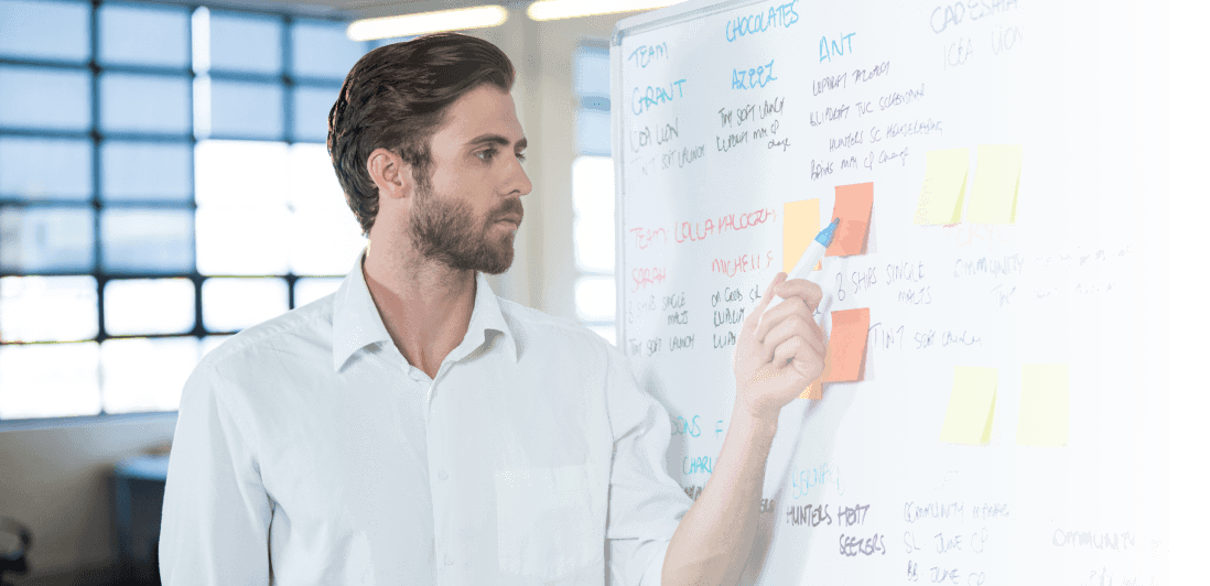 A man standing next to the whiteboard and making a plan how to scale his software development team