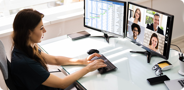 Female developer working at a monitor displaying a remote team video call