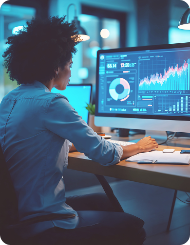 A person seated at a desk viewing multiple computer screens displaying charts, graphs, and data dashboards.